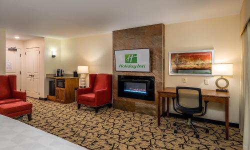 スティーブンスポイントにあるHoliday Inn Stevens Point - Convention Center, an IHG Hotelの椅子2脚と暖炉付きのホテルルームです。