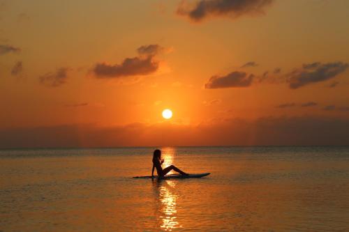 a person sitting on a surfboard in the ocean at sunset at YOISAMA Sunset Beach House in Ishigaki Island