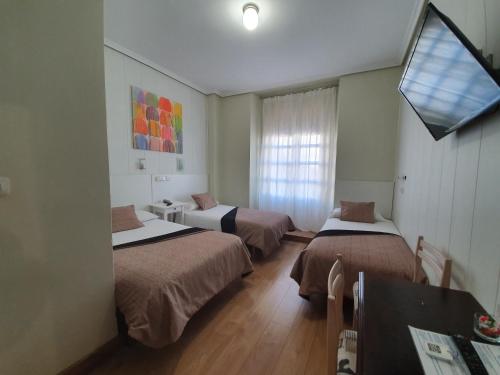 Habitación con 3 camas, mesa y TV. en Hostal Riesco, en Madrid