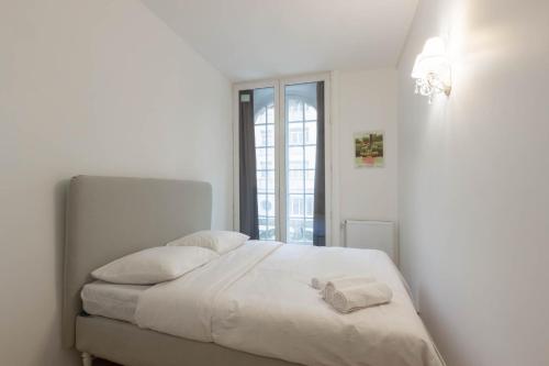 a white bedroom with a bed with white sheets and a window at Marais Renard in Paris