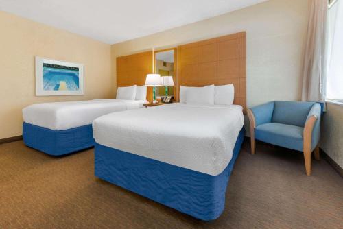 a hotel room with two beds and a chair at La Quinta by Wyndham Fort Lauderdale Pompano Beach in Fort Lauderdale