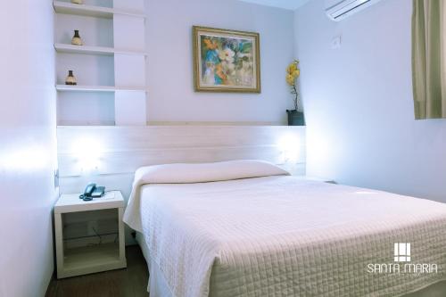 a bedroom with a white bed and a table and shelves at Hotel Santa Maria in Campo Mourão