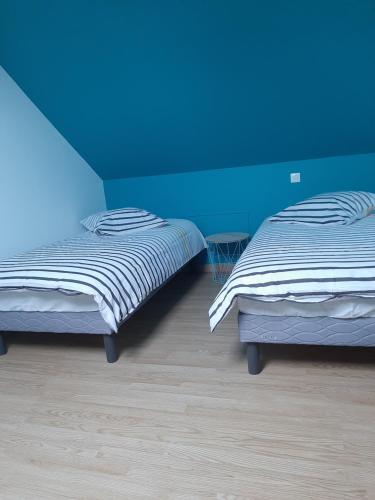 two beds in a room with a blue wall at La petite maison in Bracquemont