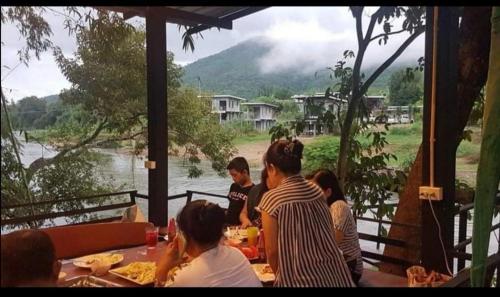 un grupo de personas sentadas en una mesa cerca de un río en Kaengkrachan River Hut en Kaeng Kachan