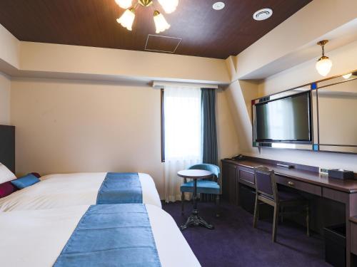 東京にあるホテル ウイング インターナショナル セレクト池袋のベッド、デスク、テレビが備わるホテルルームです。