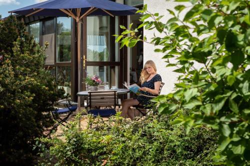 una mujer sentada en un banco leyendo un libro en Kurhotel Bad Schmiedeberg en Bad Schmiedeberg