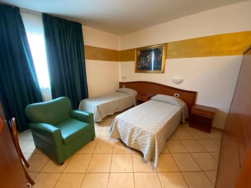 een slaapkamer met 2 bedden en een groene stoel bij Mini Hotel in Asti