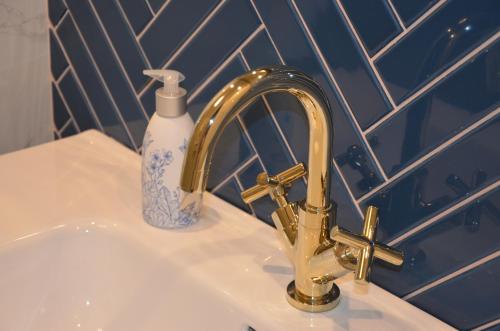 a bathroom sink with a gold faucet and a bottle of soap at Długie Ogrody Apartment 140 Gdańsk in Gdańsk