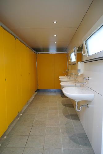 a row of sinks in a bathroom with yellow walls at Safaritent op Camping Berkel in Bockholtz