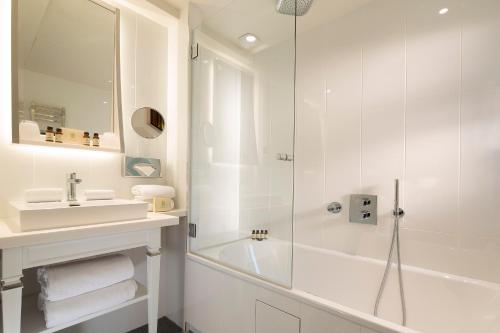 ein weißes Bad mit einer Dusche und einem Waschbecken in der Unterkunft Hôtel Baume in Paris