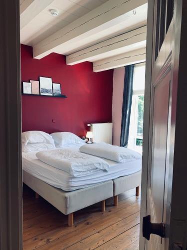 a bedroom with a large bed with a red wall at Logies De Reiziger in Groede