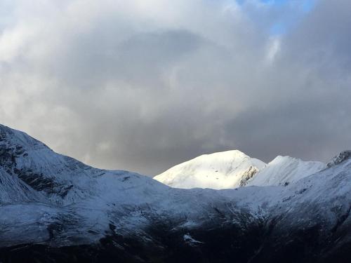 a group of snow covered mountains under a cloudy sky at Woodland Cabins, Glencoe in Ballachulish