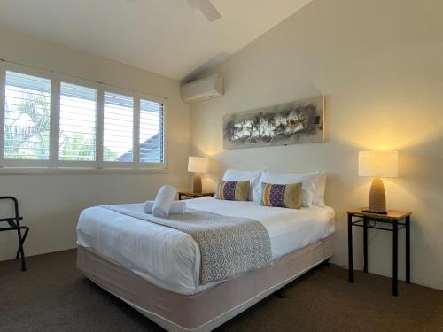 a bedroom with a large white bed and two lamps at Byron Quarter Apartments in Byron Bay