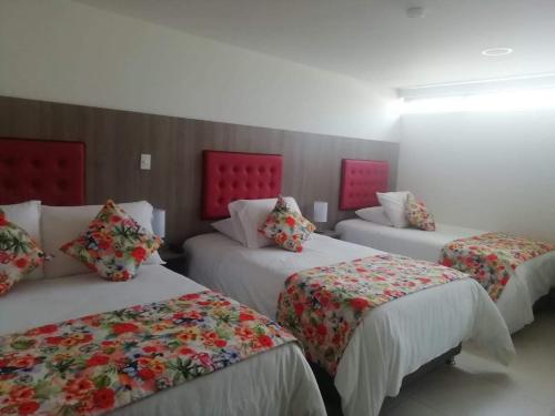 3 Betten in einem Zimmer mit roten Kopfteilen in der Unterkunft Hotel Grato Manizales in Manizales