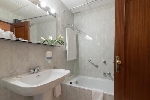 een badkamer met een wastafel, een bad en een spiegel bij Hospedium Hotel Europa Centro in Magaz De Pisuerga