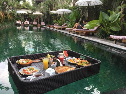 een dienblad met eten op een tafel naast een zwembad bij Sapodilla Ubud in Ubud