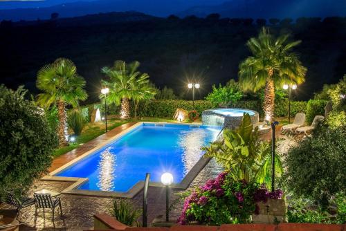 una piscina en un jardín por la noche con palmeras en B&B Le Foglie D'Argento, en Caltabellotta