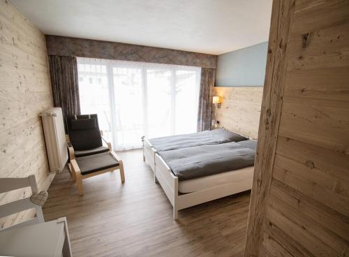 een slaapkamer met een bed, een stoel en een raam bij Hotel La Reserve in Sankt Niklaus