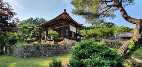 a house in a garden with a stone wall at Ahndong Kimjongtaek Yangsodang in Andong