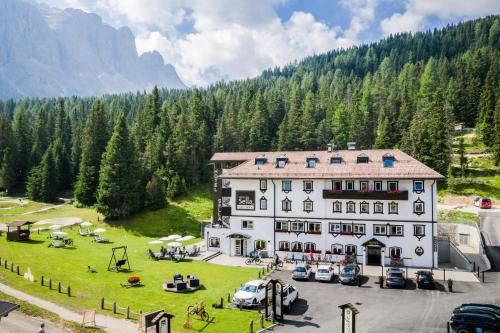 a large white building with cars parked in a field at Hotel Sella***s in Selva di Val Gardena