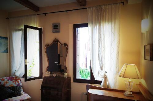 Zimmer mit 2 Fenstern, einem Spiegel und einer Lampe in der Unterkunft Cà Tron Apartment next to Rialto bridge in Venedig