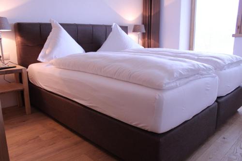 ein großes Bett mit weißer Bettwäsche und Kissen darauf in der Unterkunft Residenz Berghof Mösern in Seefeld in Tirol