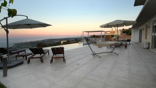 a patio with chairs and umbrellas on a house at Eva Villas West and East with 2 private infinity pool & and panoramic sea view in Gerani