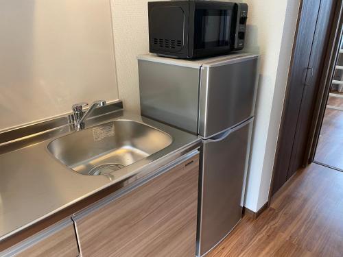 a kitchen with a sink and a microwave on top of a refrigerator at ホテルトーマス牧港ヴィラ in Urasoe