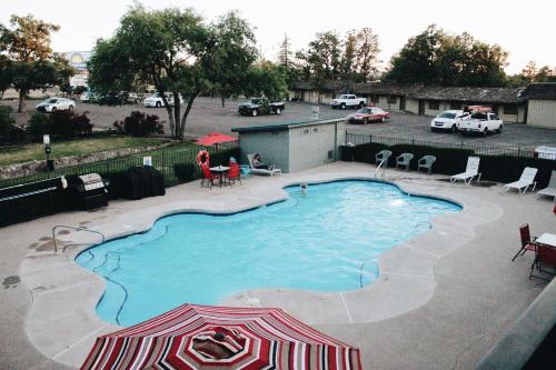 a swimming pool with an umbrella and chairs and cars at Days Inn by Wyndham Show Low in Show Low