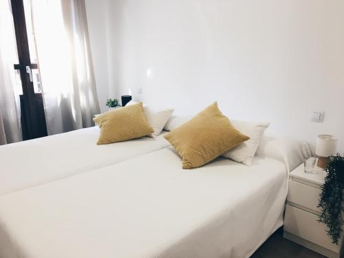 Cama blanca con sábanas blancas y almohadas amarillas en Apartamentos Pozo Amarillo, en Salamanca