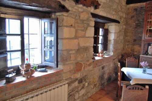 a stone kitchen with a table and two windows at La Casona de Tresgrandas in Tresgrandas