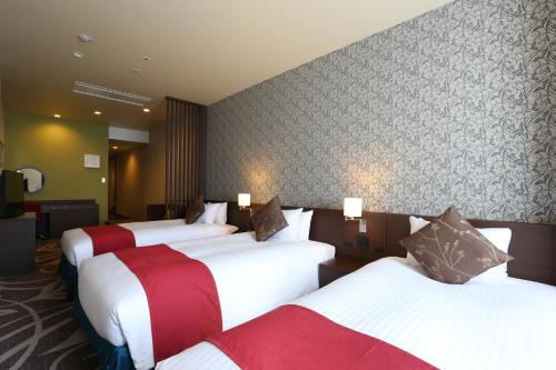a hotel room with three beds with red and white at Quintessa Hotel Osaka Bay in Osaka