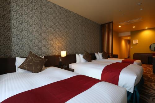 a hotel room with three beds with red and white at Quintessa Hotel Osaka Bay in Osaka