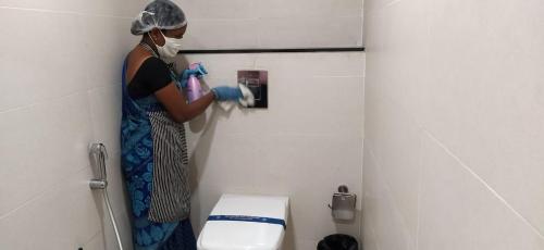 a person wearing a mask and gloves washing a toilet at Hotel Grand Gayathri in Khammam