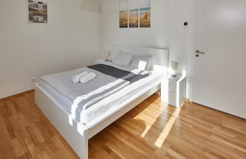 ein weißes Bett in einem weißen Schlafzimmer mit Holzboden in der Unterkunft Helle und gemütliche Wohnung in zentraler Lage in Graz