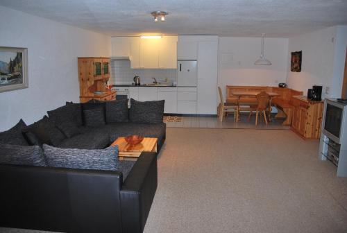 ein Wohnzimmer mit einem schwarzen Sofa und einer Küche in der Unterkunft Ferienwohnung Bürchen in Bürchen