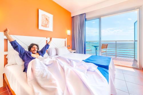 a man laying in a bed with his arms in the air at Hotel Na Forana in Cala Ratjada