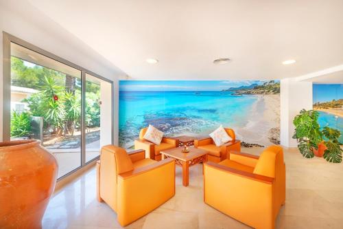 a living room with orange chairs and a painting of the beach at Hotel Na Forana in Cala Ratjada
