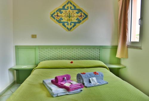 un letto verde con due paia di pantofole sopra di Casa Mare Cala Rossa a Trinità dʼAgultu