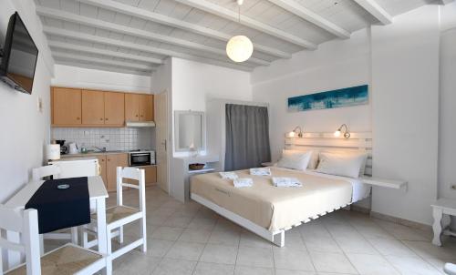 a bedroom with a white bed and a kitchen at Nostos Beachfront Apartments & Studios in Agios Ioannis