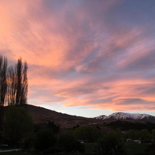 a sunset with a tree and mountains in the background at Waiorau Homestead in Cardrona