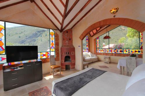 1 dormitorio con 1 cama y TV y algunas ventanas en Suites Arcoiris, en Villa de Leyva