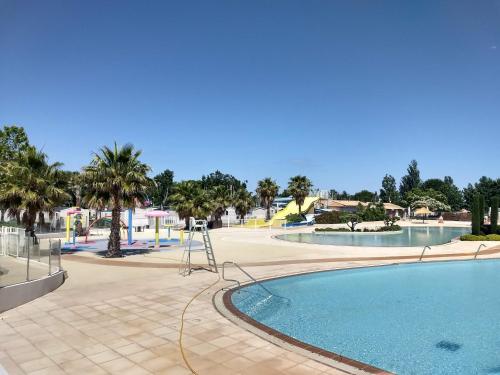a pool at a park with palm trees and a playground at VIAS Plage La Carabasse - Mobile home 6 places in Vias