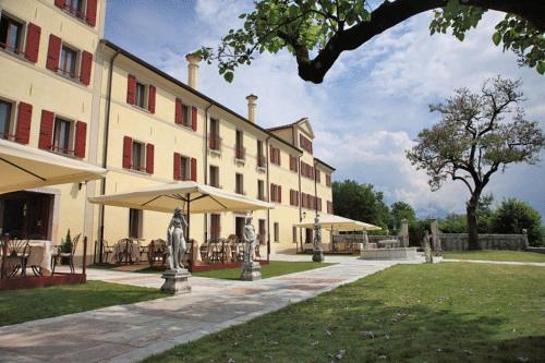 a large building with tables and umbrellas in front of it at Park Hotel Villa Carpenada in Belluno