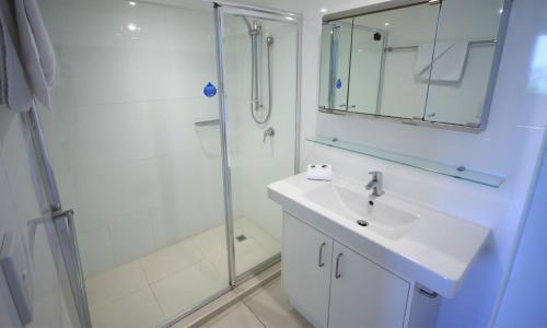 Un baño blanco con lavabo y ducha. en San Simeon Beachfront Apartments Tugun, en Gold Coast