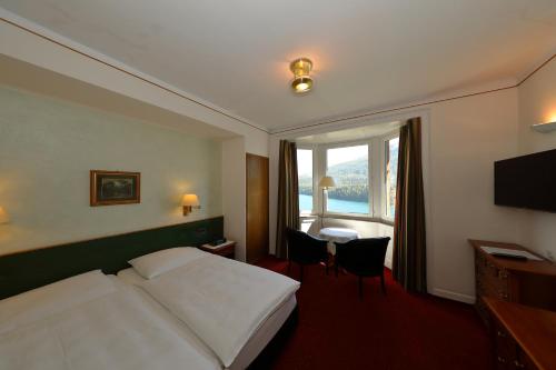 um quarto de hotel com uma cama, uma secretária e uma janela em Soldanella em St. Moritz