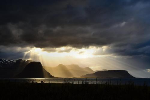 a stormy sky with the sun shining between two mountains at Sudur-Bár Guesthouse in Grundarfjordur