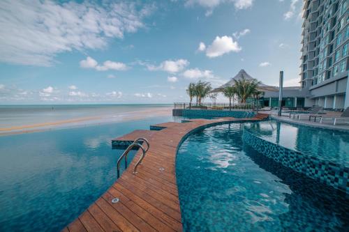 a swimming pool next to a beach and a building at Swiss-Belhotel Kuantan in Kuantan