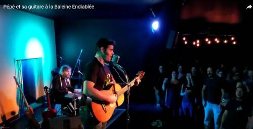 a man playing a guitar in front of a audience at La Baleine Endiablée Microbrasserie in Rivière-Ouelle