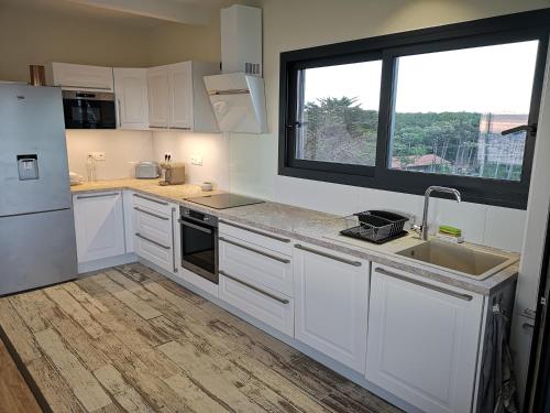 eine Küche mit weißen Schränken und einer Spüle und einem Fenster in der Unterkunft Les Terrasses de l'Océan in Mimizan